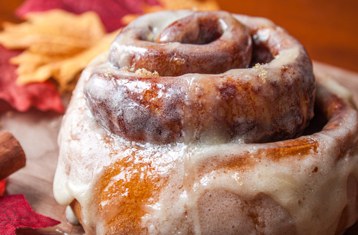 close-up image of a cinnamon roll with frosting and a festive fall background