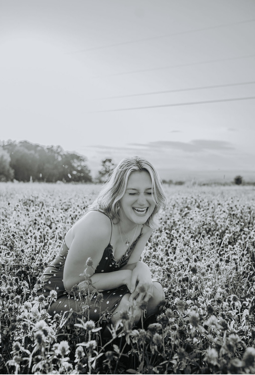 A girl sitting and laughing in a field full of flowers.